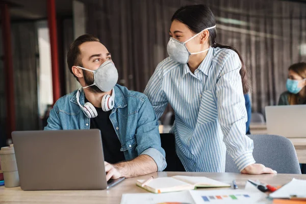 Foto Estudantes Alegres Multinacionais Máscaras Médicas Estudando Com Laptop Sala — Fotografia de Stock