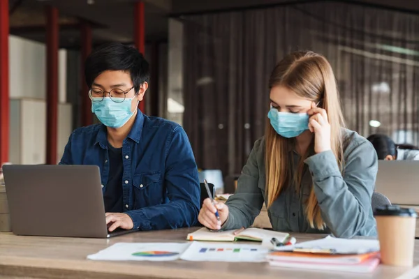 Foto Jovens Estudantes Multinacionais Máscaras Médicas Estudando Com Laptop Sala — Fotografia de Stock