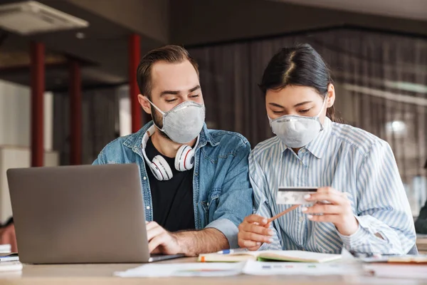 Foto Estudantes Multinacionais Agradáveis Máscaras Médicas Segurando Cartão Crédito Enquanto — Fotografia de Stock