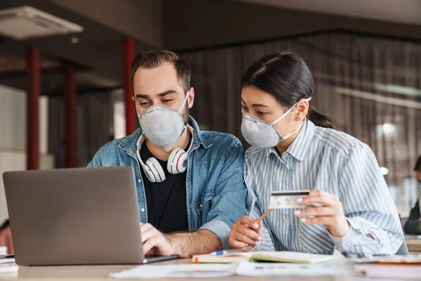 Foto Estudantes Multinacionais Agradáveis Máscaras Médicas Segurando Cartão Crédito Enquanto — Fotografia de Stock