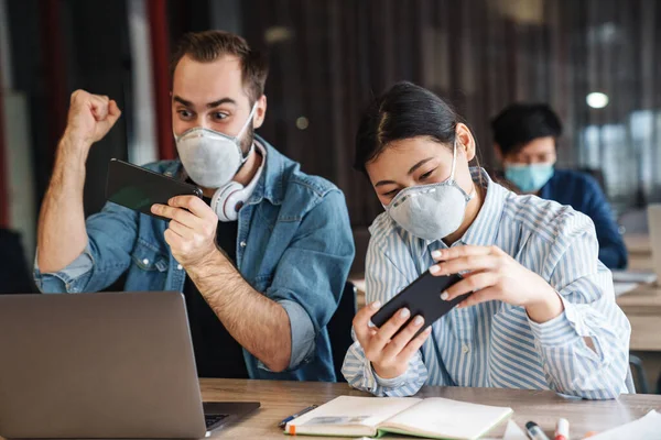 Foto Estudantes Excitados Multinacionais Máscaras Médicas Jogando Videogame Celulares Enquanto — Fotografia de Stock