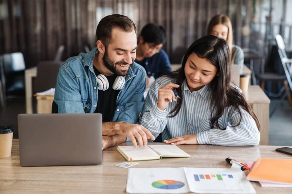 Foto Estudiantes Alegres Multinacionales Usando Laptop Escribiendo Cuaderno Ejercicios Mientras — Foto de Stock