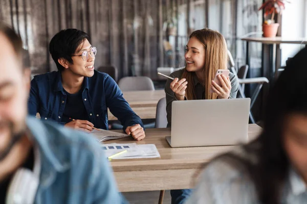 Foto Estudiantes Multinacionales Alegres Hablando Usando Teléfonos Inteligentes Mientras Estudian — Foto de Stock