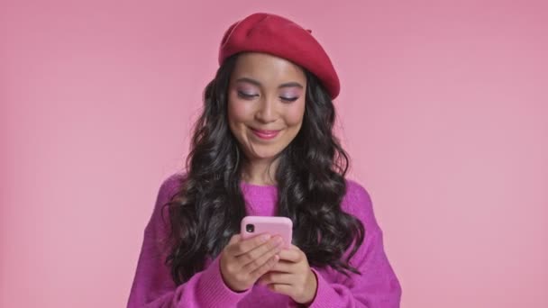 若いです正アジアの女性Posing絶縁上ピンク壁背景使用して携帯電話 — ストック動画