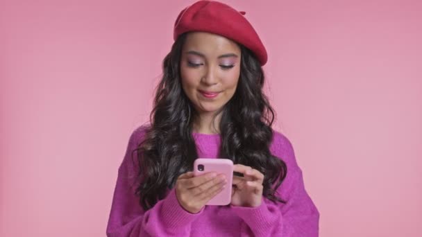 年轻快乐的亚洲女人在粉红的墙壁上摆出孤身一人的姿势 用手机做得奖手势 — 图库视频影像