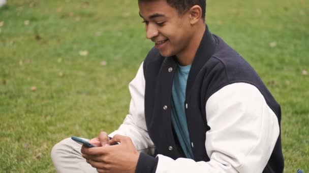 Concentrado Joven Alegre Sonriente Africano Chico Estudiante Utilizando Teléfono Móvil — Vídeos de Stock