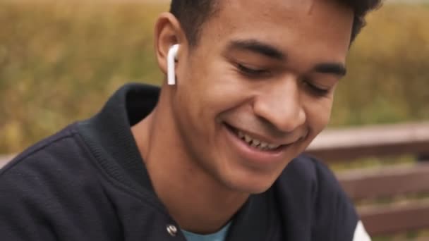在公园里 年轻英俊快乐的非洲小伙子学生在户外用无线耳机听音乐 — 图库视频影像