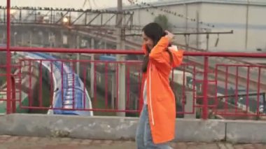 Güzel Asyalı gülümseyen pozitif kadın liman kenarında yürüyen turuncu ceketli açık hava bursu.