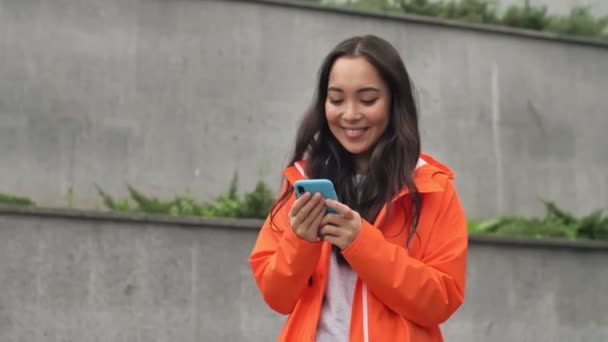 Muito Asiático Otimista Mulher Positiva Livre Casaco Laranja Usando Telefone — Vídeo de Stock