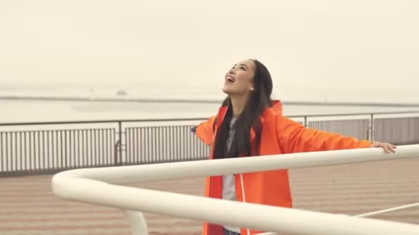 穿着橙色外套 高举双手 走在港口外的漂亮的亚洲快乐积极的女人 — 图库视频影像