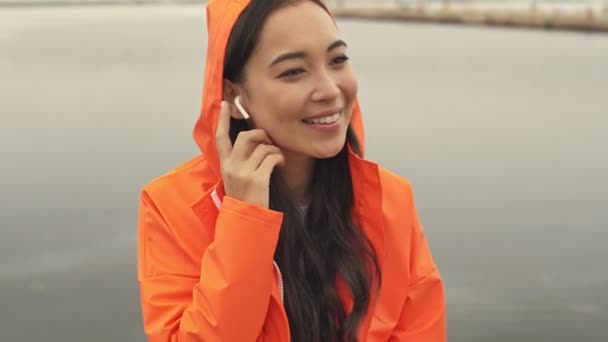 Hübsche Asiatische Positive Frau Die Orangefarbenen Mantel Hafen Vorbeiläuft Und — Stockvideo