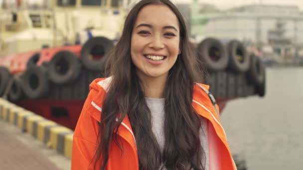 美丽的亚洲快乐的积极女子穿着橙色外套 笑着走过港口赠与 — 图库视频影像