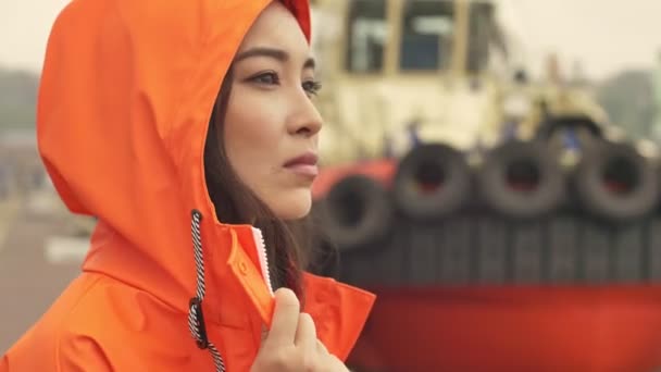 항구를 걸으며 오렌지 코트를 밖으로 나가는 중심적 이시아인 — 비디오