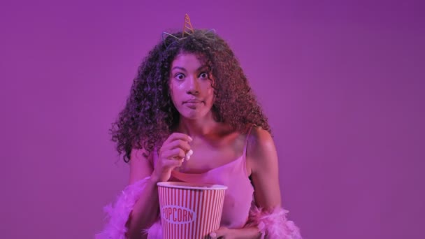 濃縮された若いアフリカの女性はネオン紫色のライトウォッチフィルム上に隔離ポップコーンを食べる — ストック動画