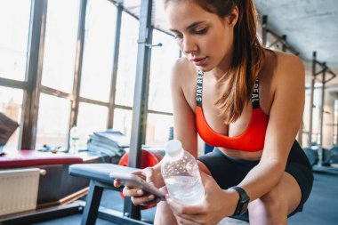 Spor salonunda spor yaparken cep telefonu ve su şişesi kullanan iyi bir sporcunun portresi.