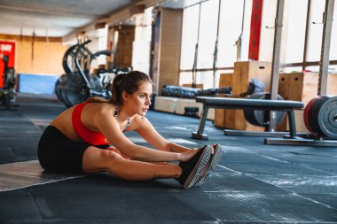 Kendine güvenen genç sporcu kadın spor salonundaki spor minderinin üzerinde esneme egzersizleri yapıyor.