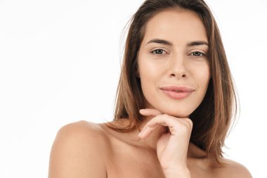 Çekici, gülümseyen üstsüz bir kadının güzel portresi beyaz arka planda izole bir şekilde duruyor, yüzüne dokunuyor, poz veriyor.