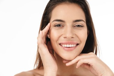 Çekici genç esmer kadın portresi yarı çıplak gülümseyen ve yüzüne dokunan beyaz arka planda izole edilmiş.