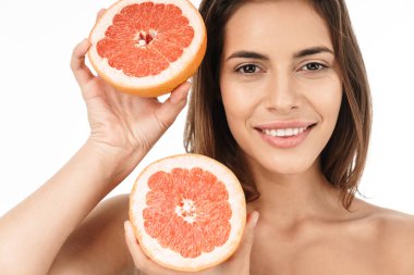 Çekici, gülümseyen, üstsüz bir kadının portresi beyaz arka planda soyutlanmış, dilimlenmiş greyfurtu gösteriyor.