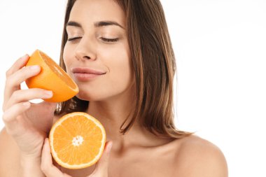 Çekici, gülümseyen, üstsüz bir kadının portresi beyaz arka planda izole bir şekilde duruyor, dilimlenmiş turuncu gösteriyor.