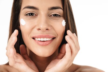 Güzel, yarı çıplak bir kadının portresi gülümseyen ve beyaz arka planda izole edilmiş yüz kremi süren.