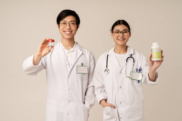 Image of asian young doctors in uniform holding pills and medicaments isolated over beige background
