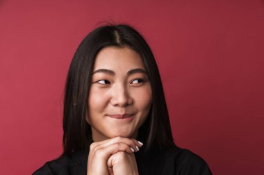 Oldukça düşünceli, genç Asyalı bir kadının kırmızı arka planda tek başına dikilip bakışlarını kaçırmasını.