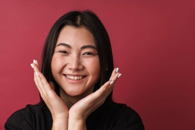 Asyalı, mutlu, genç bir kadının kırmızı duvar arkasında yalnız poz vermesi..