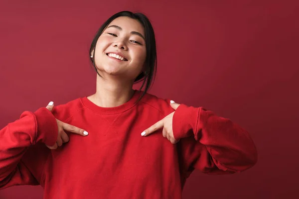 一个穿着休闲装 面带微笑的年轻亚洲女人站在近旁 与红色背景隔离 用手指指着自己 — 图库照片