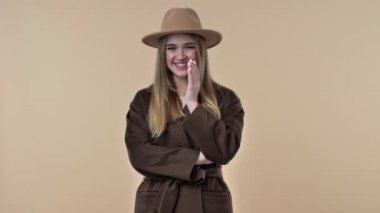 Şapka ve ceket giyen sevimli bir genç kız stüdyoda izole edilmiş bir şekilde kameraya gülümsüyor.