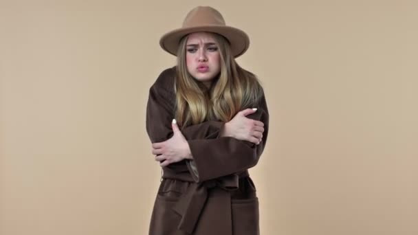 一位戴着帽子和外套的年轻貌美女子在工作室的米色背景下感到很冷淡 — 图库视频影像