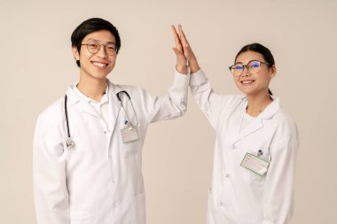 Beyaz üniformalı Asyalı genç tıp doktorlarının bej arka planda beşlik çakışları.