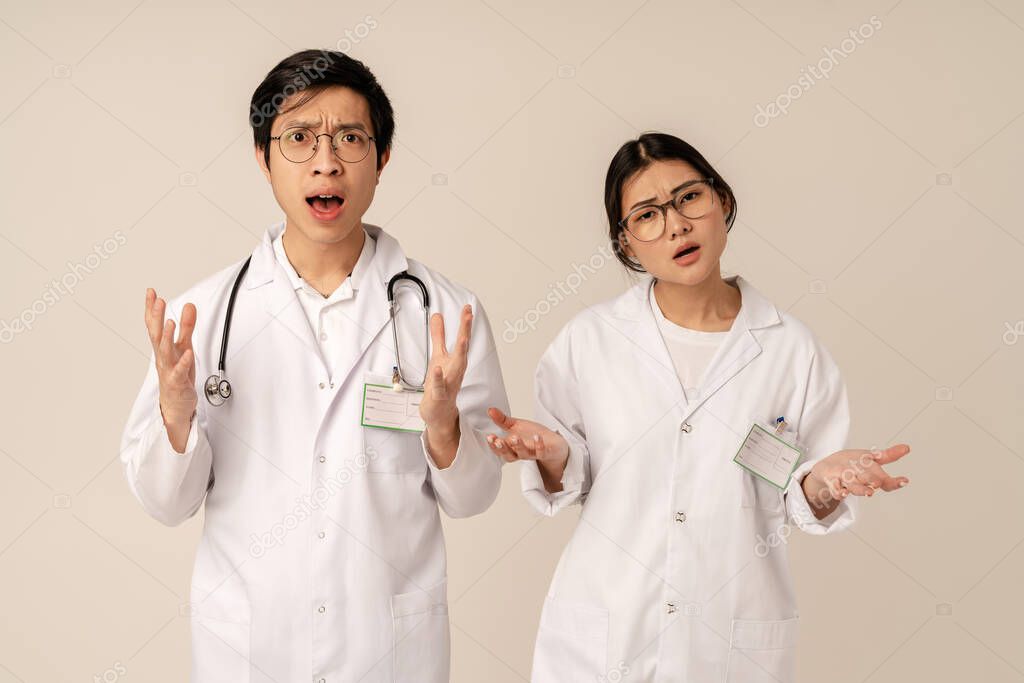 Image of asian young medical doctors in white uniform expressing outrage during viral disease isolated over beige background