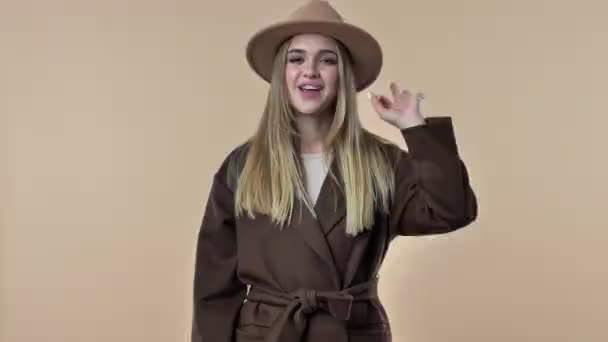 Положительная Улыбающаяся Молодая Женщина Шляпе Пальто Показывает Хороший Жест Бежевом — стоковое видео