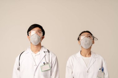 Beyaz üniformalı ve koruyucu maskeli Asyalı genç doktorların bej arka planda izole edilmiş görüntüsü.