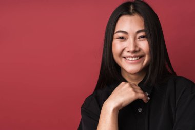 Kırmızı arka planda dikilip kameraya bakan, sıradan giyinmiş, güzel gülümseyen Asyalı genç bir kadının fotoğrafını çek.