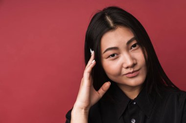 Kırmızı arka planda tek başına duran, sıradan kıyafetler giyen, düşünceli, genç bir Asyalı kadının fotoğrafını çek.