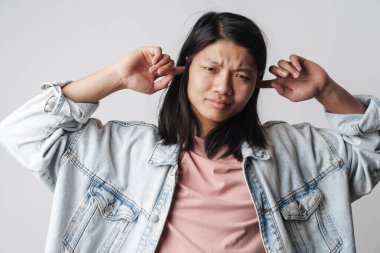 Hoşnutsuz Asyalı adamın görüntüsü kameraya bakıyor ve kulaklarını beyaz arka planda izole ediyor.