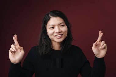 Neşeli Asyalı bir adamın gülümsemesi ve şans dilemek için parmaklarını çaprazlaması burgonya arka planında izole edilmiş.