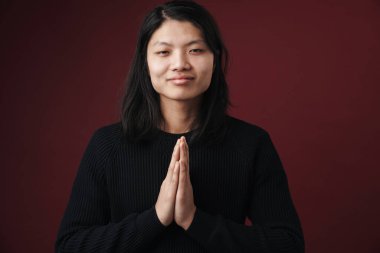 Kamerada gülümseyen Asyalı bir adam resmi. Avuç içleri birbirine kenetlenmiş. Burgonya arka planında izole edilmiş.