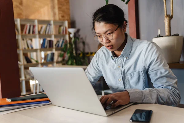 Imagem Homem Asiático Bonito Focado Óculos Estudando Com Laptop Enquanto — Fotografia de Stock