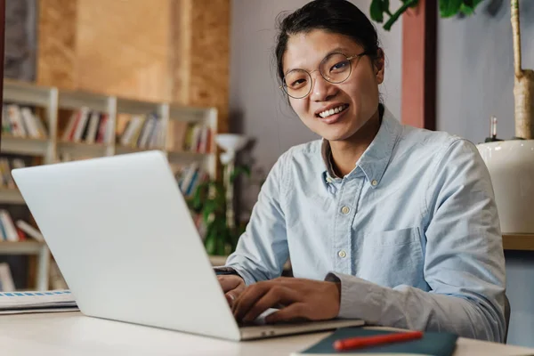 満足そうなハンサムなアジア人男のイメージで眼鏡笑顔と勉強ノートパソコンと一緒に座ってテーブル — ストック写真