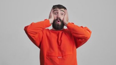 Genç, şok olmuş esmer adam, gri duvar arkasında izole edilmiş..