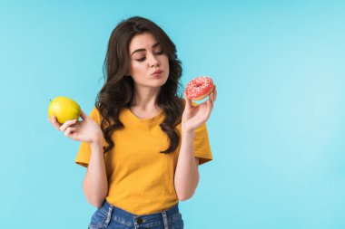 Elma ve donut taşıyan genç ve güzel bir kadının mavi duvar arkasında yalnız poz vermesi..