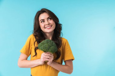 Elinde brokoli olan, mavi duvar arkasında izole bir şekilde poz veren hoş ve güzel bir kadın resmi..