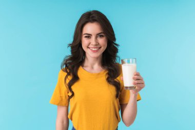 Mavi duvar arkasında elinde sütle yalnız poz veren mutlu, pozitif iyimser genç kadın görüntüsü..