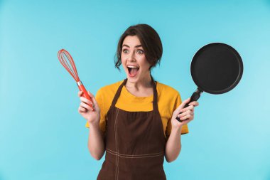 Sevimli, heyecanlı, genç bir kadın aşçının elinde çırpı ve kızartma tavasını mavi duvarın arkasında izole bir şekilde tutması..