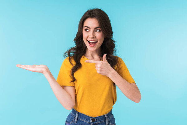 Image of a happy optimistic cheery young pretty woman posing isolated over blue wall background pointing.