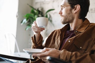 Gözlük takan yakışıklı, tıraşsız bir gencin parlak, modern bir kafede dinlenirken çay içişi.