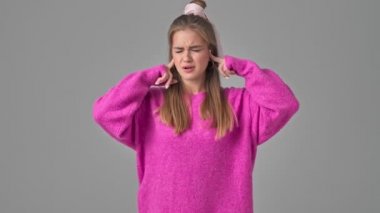 Çekici genç bir kadın kulaklarını kapatırken stüdyodaki gri bir arka plandan izole edilmiş anlamsız bir içeriği gösteriyor.